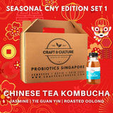 Craft & Culture's promotional image for the Chinese Tea Series - The Classics - Kombucha Set 1 features a cardboard box and a bottle of kombucha in Jasmine Green Tea, Tie Kuan Yin, and Roasted Oolong flavors amid red and gold festive decorations.